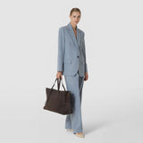 Front view: A woman carries the MAXI MARO BAG IN SUEDE AND MOSAICO by its long handles; the dark brown bag features textured Mosaico details and suede.