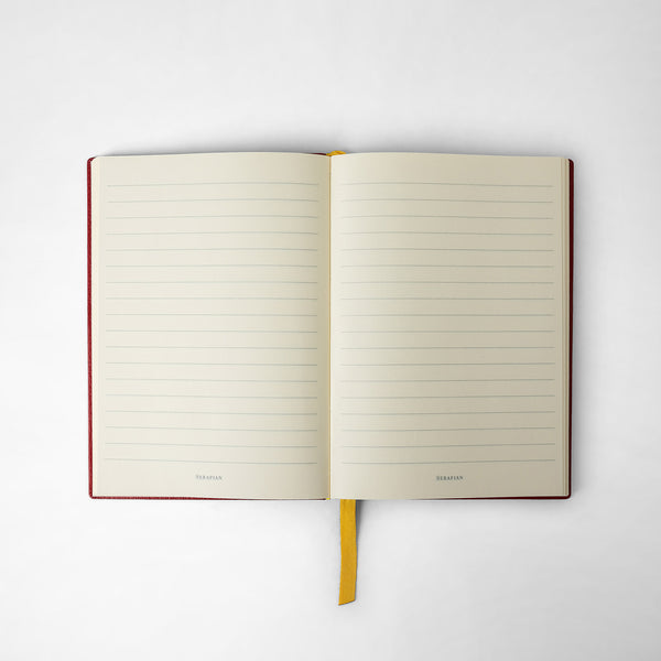 Front view of an open NOTEBOOK IN CACHEMIRE LEATHER with lined pages, amaranth leather cover, and yellow ribbon bookmark, with &#39;SERAPIAN&#39; text at the bottom.