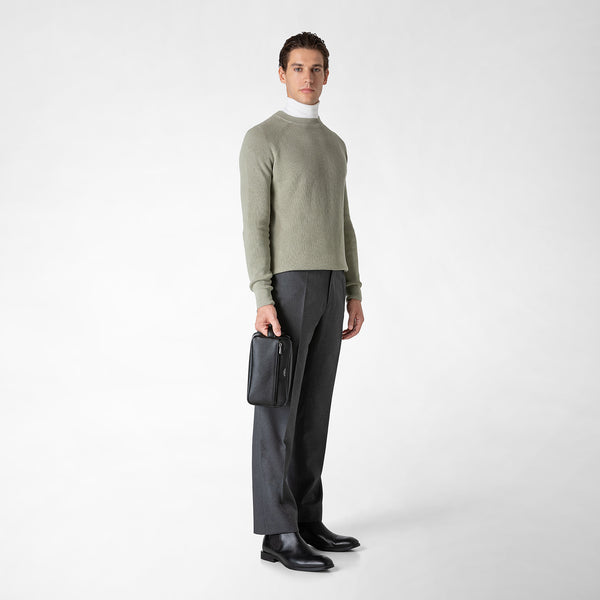 Front view of a man holding the WASHBAG IN EVOLUZIONE LEATHER in eclipse black in his right hand, while elegantly dressed.