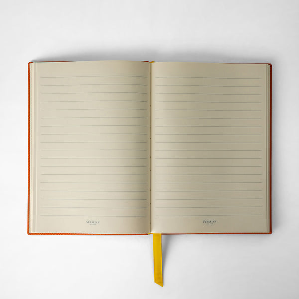 Front view of open NOTEBOOK IN EVOLUZIONE LEATHER with flame-colored leather cover, lined pages, yellow ribbon bookmark, and Serapian logo at bottom of both pages.
